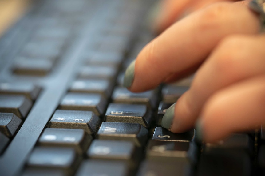 Tangan kiri seorang wanita menekan tombol berhuruf pada keyboard komputer dengan jari-jari yang telah dicat kuku.