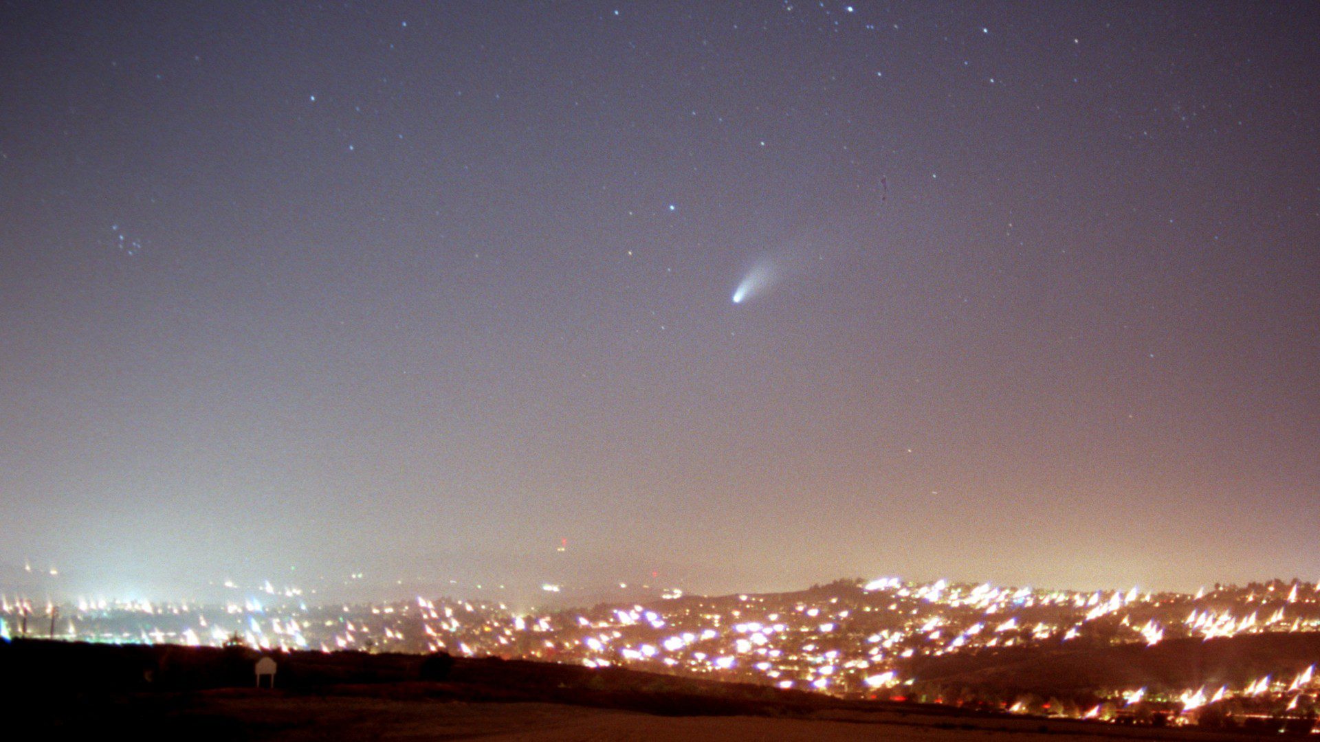 Sebuah komet terang di atas bidang lampu kota yang terang