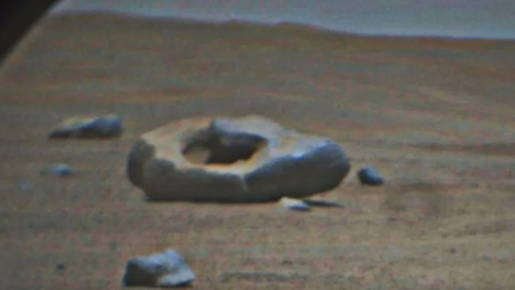 large black rock with a hole in its center sitting on mars