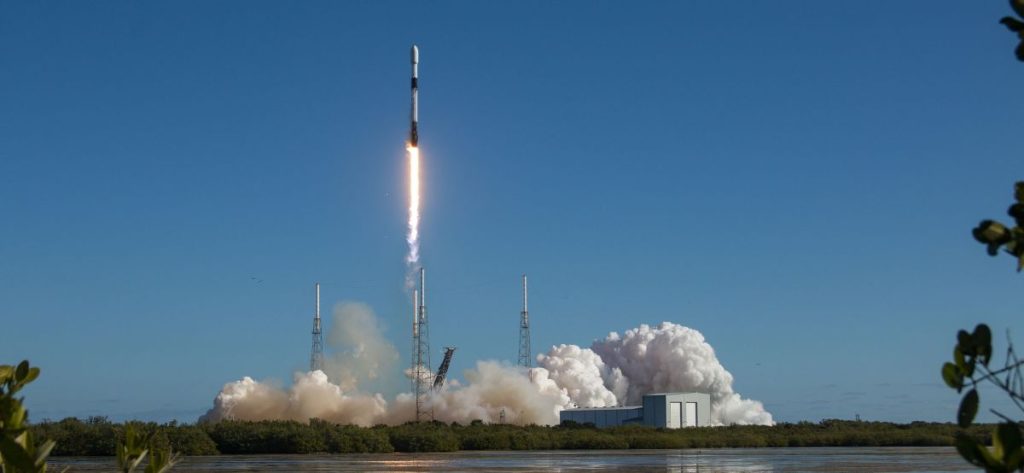 A black-and-white spacex falcon 9 rocket launches into a clear blue sky.