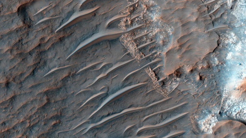 view of mars from orbit showing reddish-brown sand dunes rippling across a rocky surface