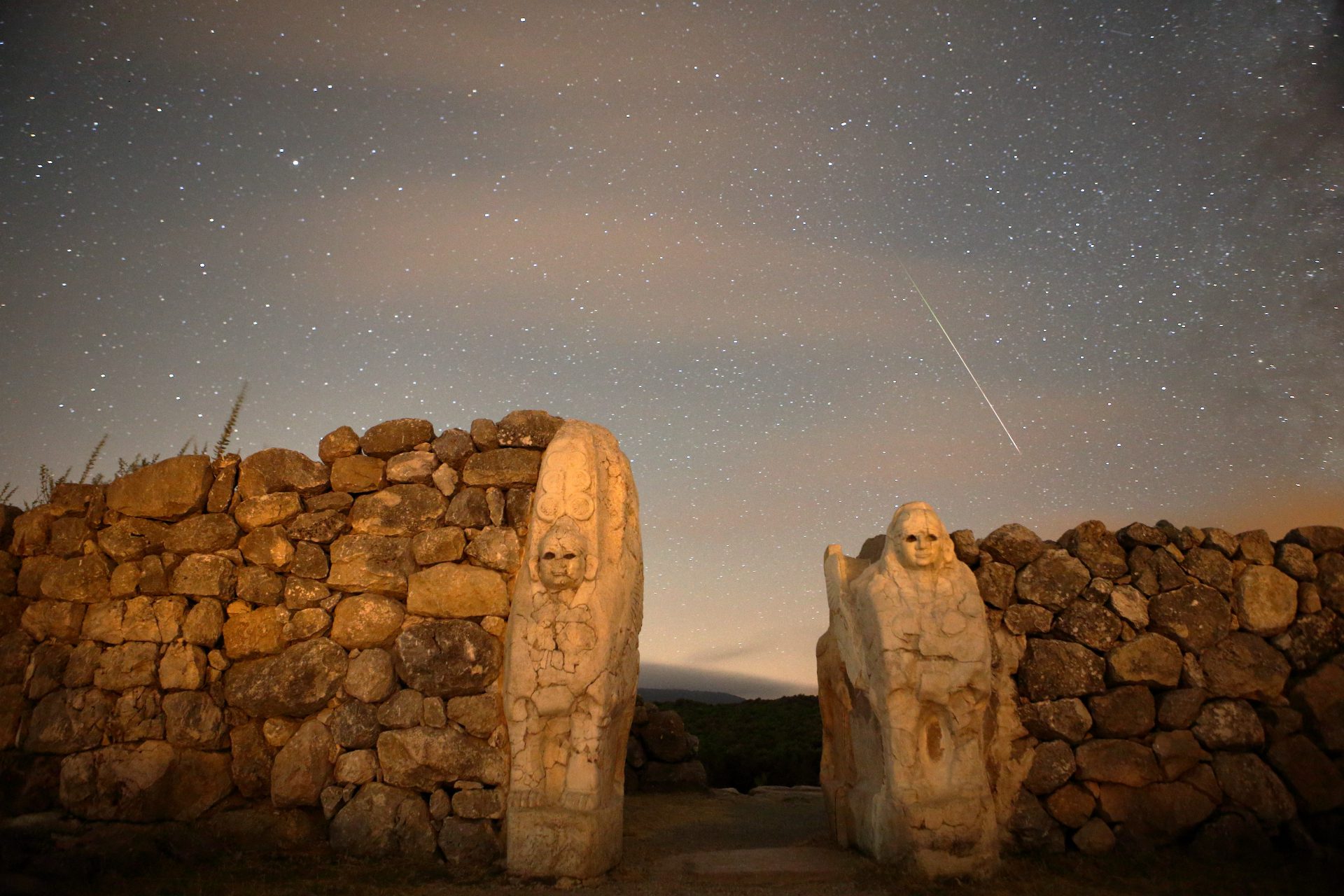 Garis meteor menonjol di langit di atas dinding batu dengan dua sosok diukir di batu.