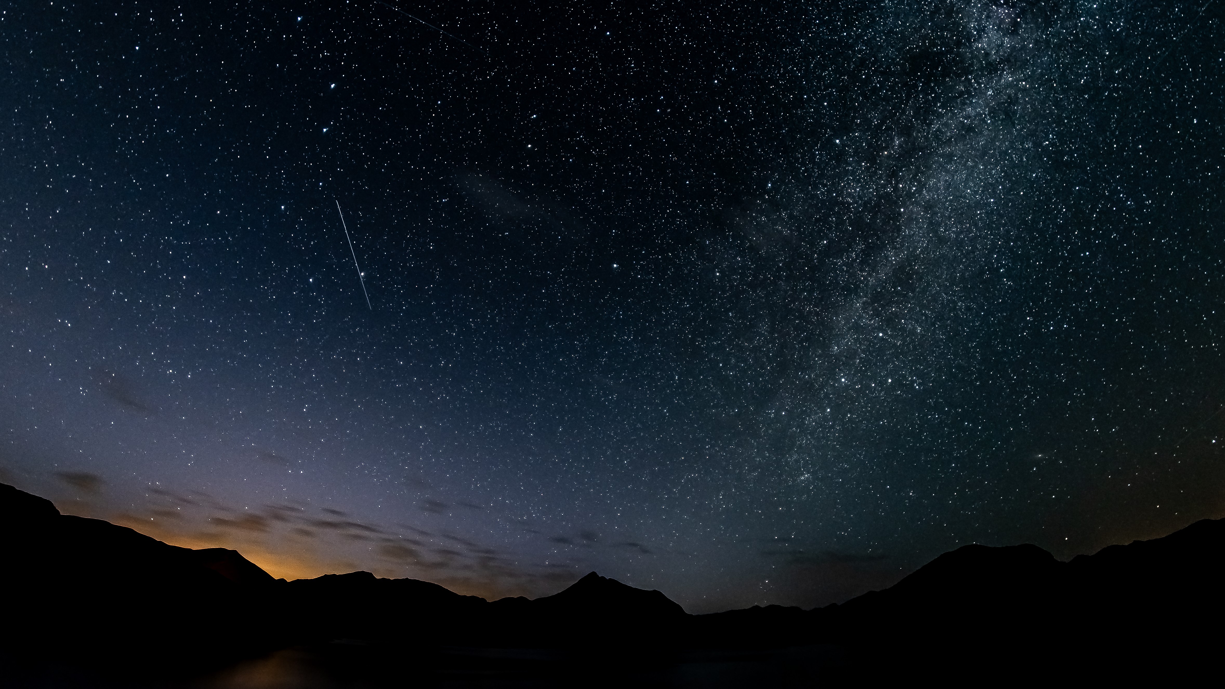 Meteor jatuh melintasi langit yang penuh bintang.