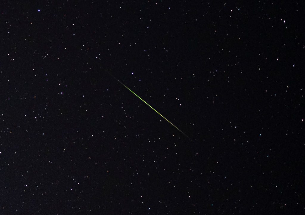 Close-up dari garis meteor hijau dan putih terang melintasi langit berbintang.