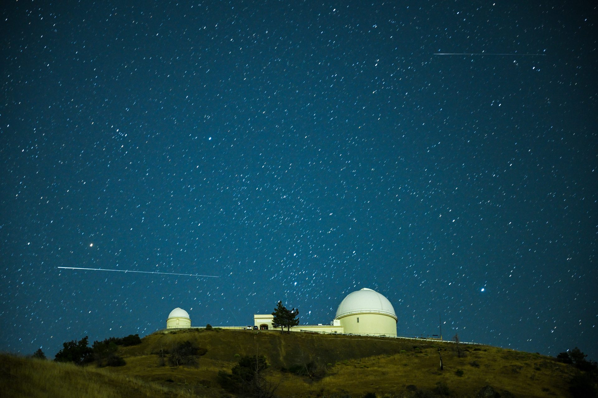 Kereta putih panjang meteor Perseid melewati struktur kubah Observatorium Danau dalam arah horizontal dengan latar langit berbintang.