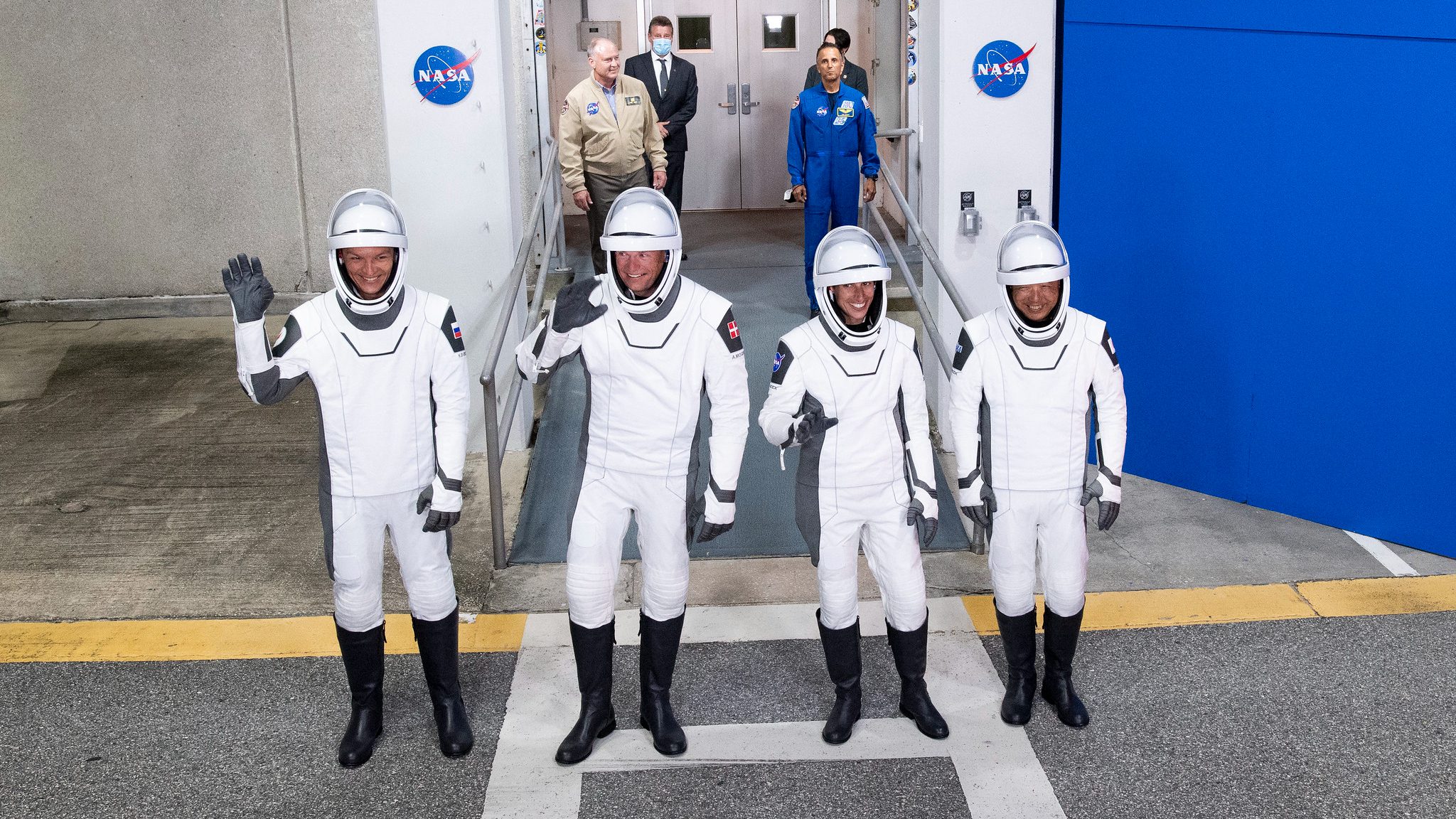 Empat astronot dengan pakaian antariksa hitam putih melambai saat mereka menuju landasan peluncuran
