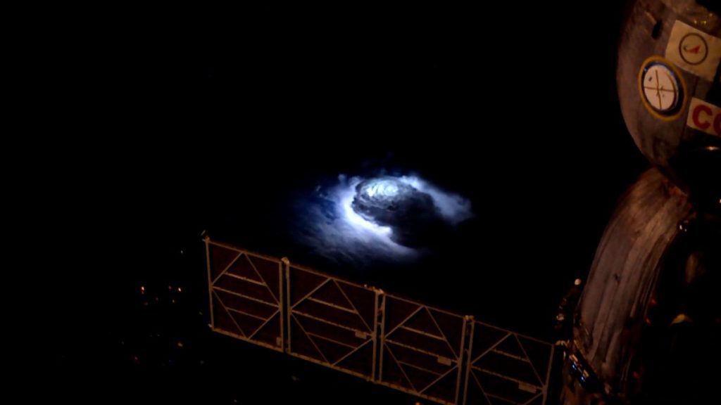 a dark thunderstorm lights up the night side of earth, as seen from the space station