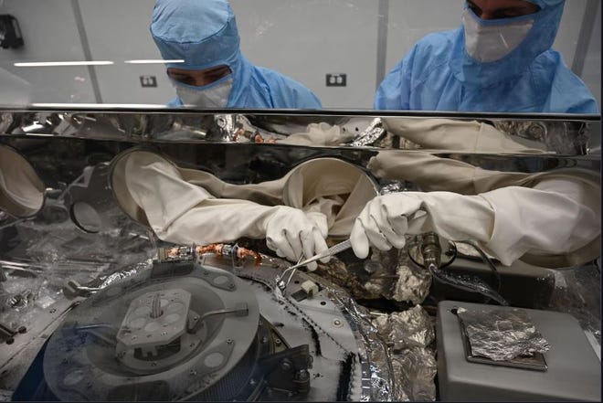 Penangan material astronomi Mary Montoya, kiri, dan Curtis Calva, kanan, menggunakan instrumen untuk mengumpulkan partikel asteroid dari dasar kandang sains OSIRIS-REx.