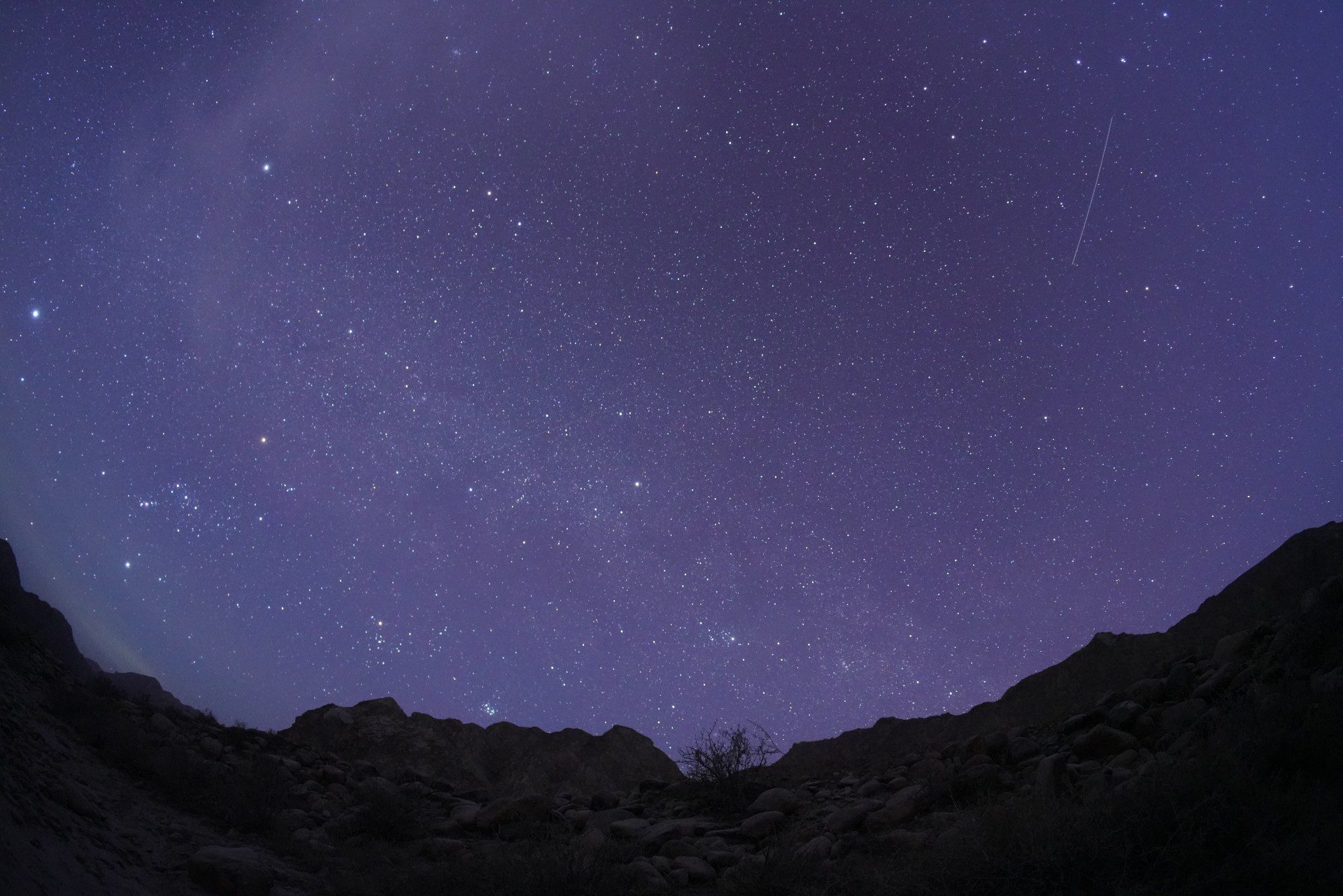 Sebuah meteor melesat menembus langit berbintang di atas pegunungan