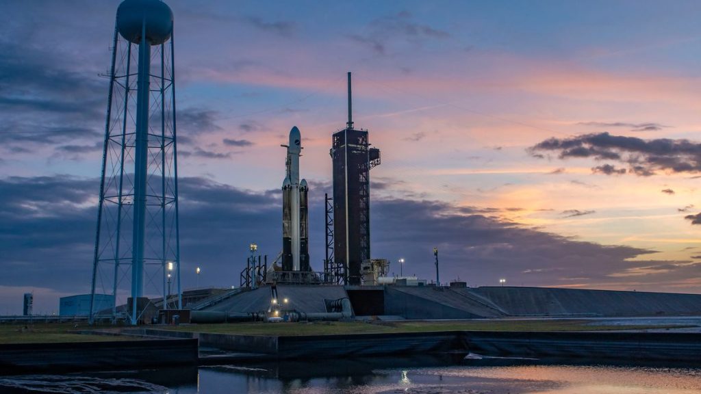 a white rocket stands on the launch pad at dusk.