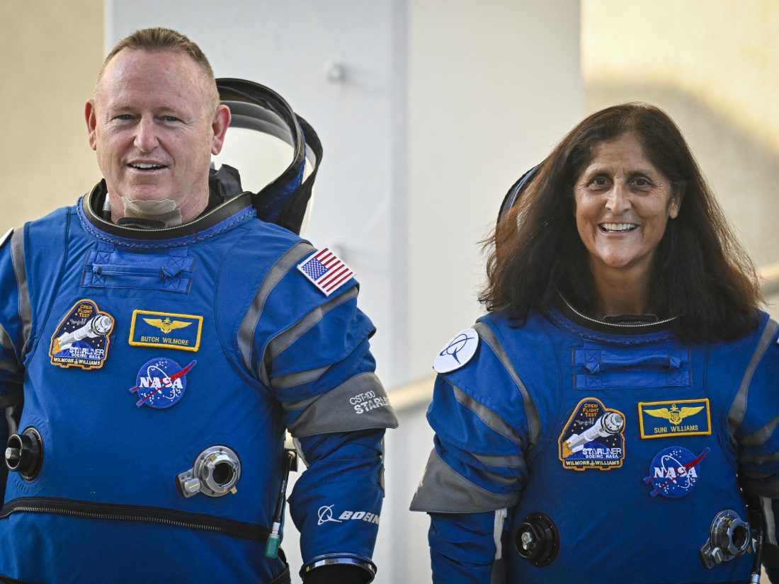 Astronot NASA Butch Wilmore (kiri) dan Sonny Williams mengenakan pakaian antariksa Boeing saat mereka meninggalkan gedung operasi dan keluar dari landasan peluncuran pada hari Rabu di Kennedy Space Center di Florida.  Ini merupakan perjalanan ketiga ke luar angkasa bagi keduanya.