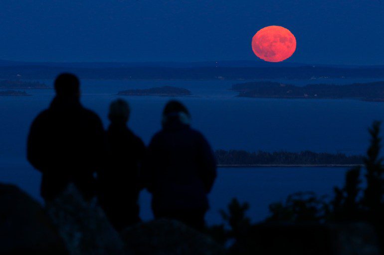 Tiga orang menyaksikan bulan panen yang hampir purnama muncul di Teluk Penobscot