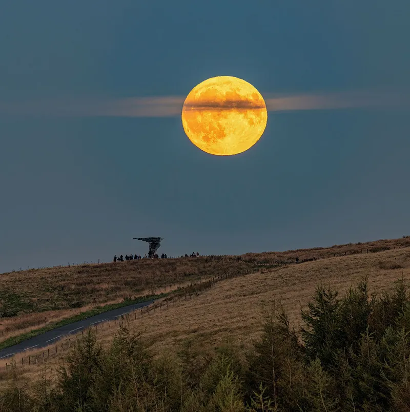 Harvest Moon dibedah awan pada 18 September 2024, diambil oleh Lee Mansfield di atas patung Singing Ringing Tree, Burnley, Lancashire, Inggris. Singing Chime Tree adalah patung akustik bertenaga angin yang menyerupai pohon yang terletak di lanskap Pennine Hills yang menghadap Burnley, di Lancashire.