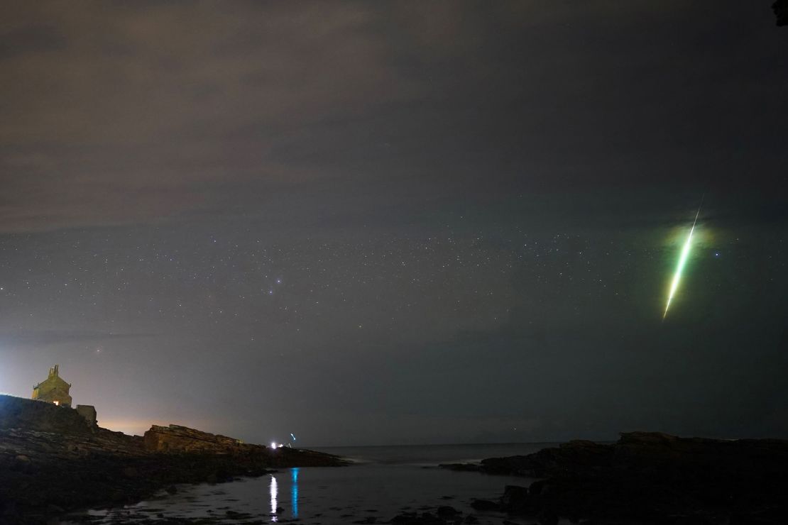 Sebuah meteor melintas di langit selama hujan meteor Draconid seperti yang terlihat di atas Howick Rocks di Northumberland di timur laut Inggris pada Oktober 2021.